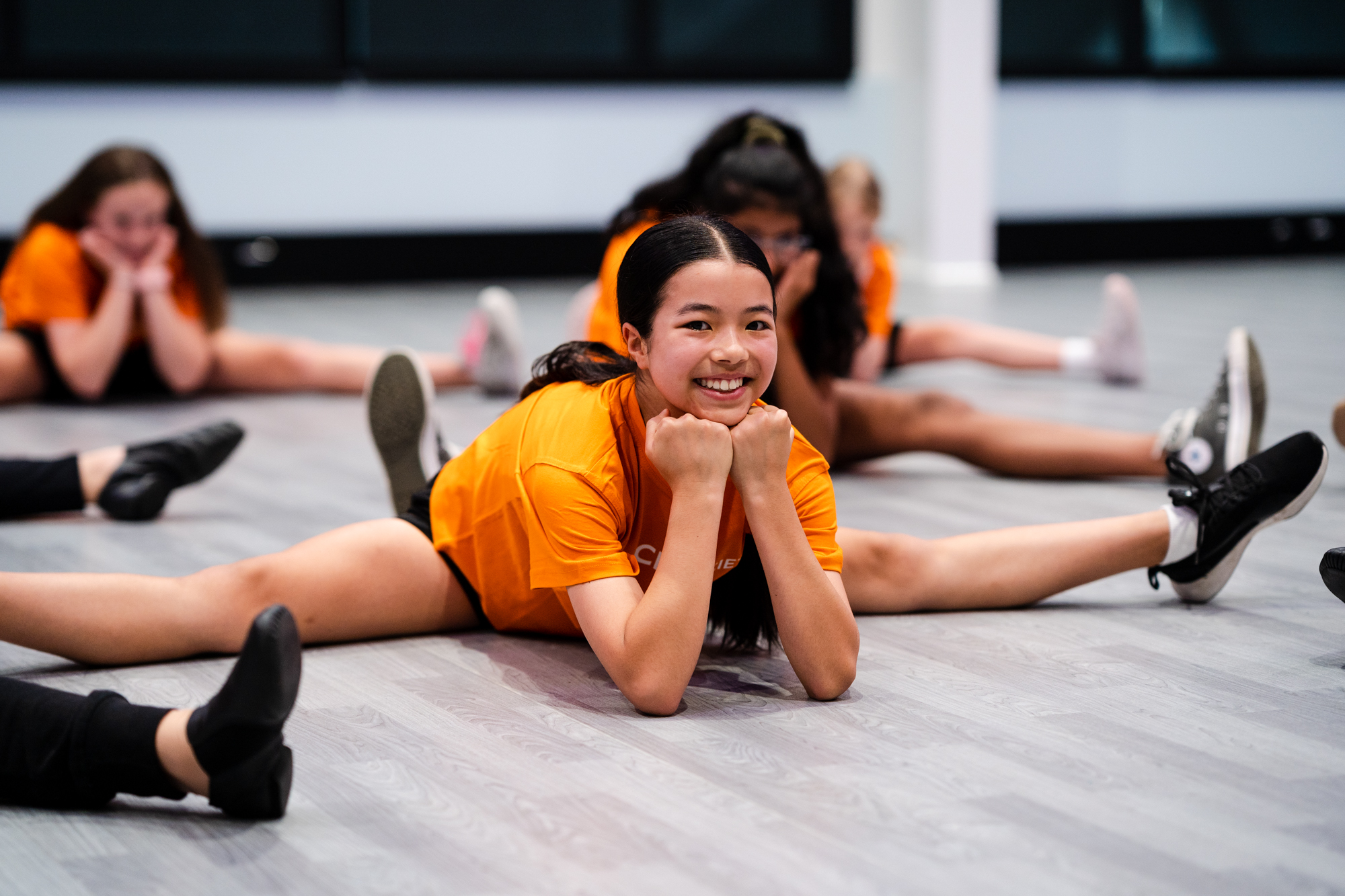 Photo of teenage girl wearing orange tee shirts in split formation with chin resting on her closed inward fist